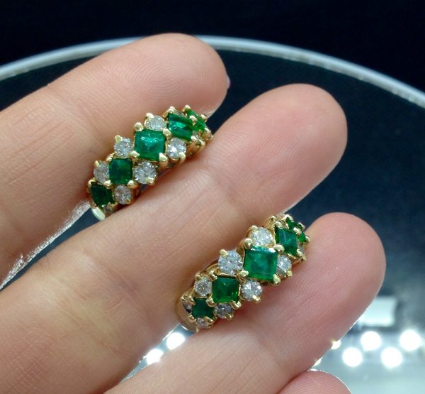 A woman holding two 0.78 Ct Colombian Emerald with 0.75 Ct Diamond 18k Yellow Gold Huggies Cocktail Earrings