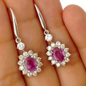 A person holding two 14K White Gold 2.0 CT Pink Sapphire Flower Earrings W/ 1.04 CT VS Diamond Halo
