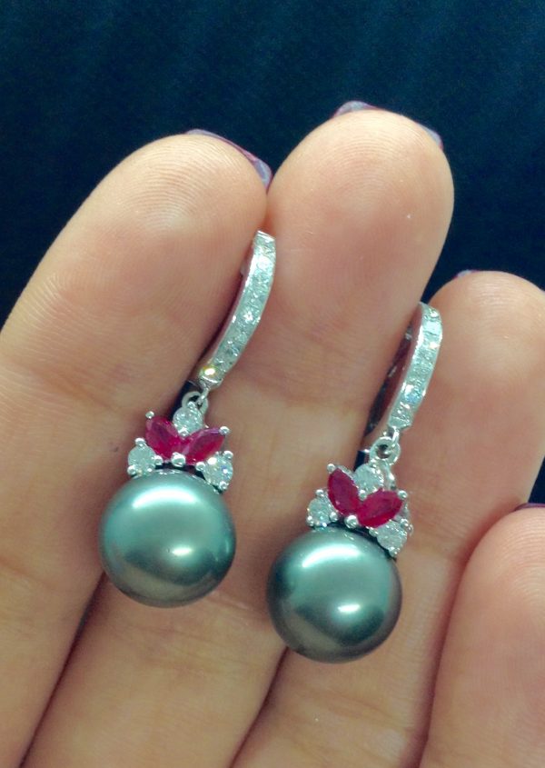 A woman holding two 18k White Gold Short Drop Tahitian 11mm Pearl with 0.85 Ct Diamonds and 0.60 Ct Ruby