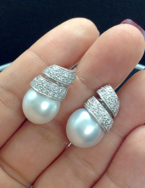 A woman holding two pieces 14mm South Sea Pearl 18k White Gold Earring with 1.25 Ct Diamond with a Twirling Design