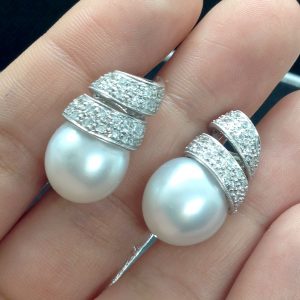 A woman holding 14mm South Sea Pearl 18k White Gold Earring with 1.25 Ct Diamond with a Twirling Design