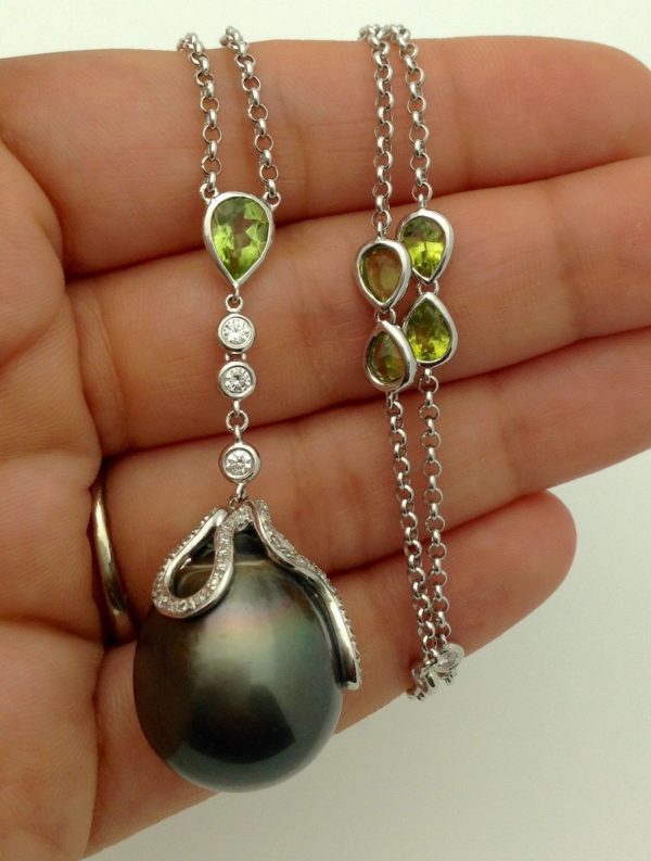 A person holding a Tahitian Pearl w/ Peridot Accents & 1.00 CT VS Diamonds 14k White Gold Necklace